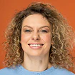 Portrait of a woman with curly brown hair smiling at the camera against an orange background.
