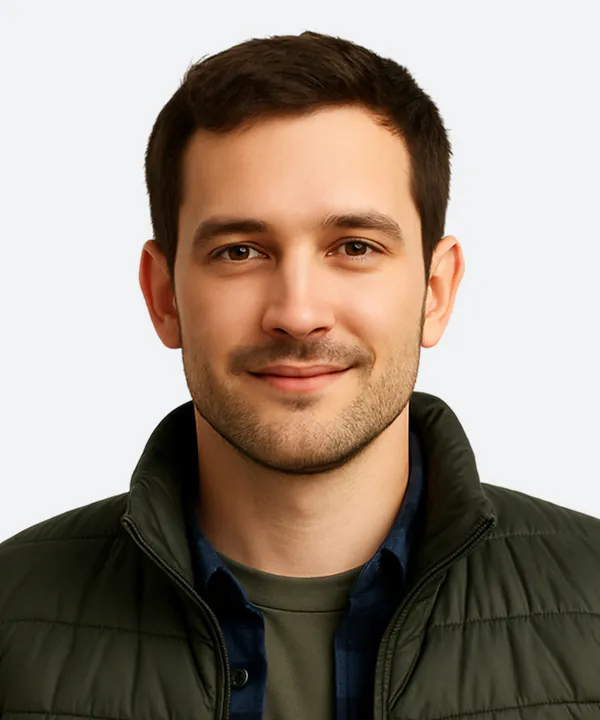 Professional headshot of a man with dark hair and facial stubble, wearing a dark green jacket over a blue shirt.