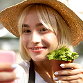 Woman wearing a straw hat holding fresh green vegetables and smiling at the camera.