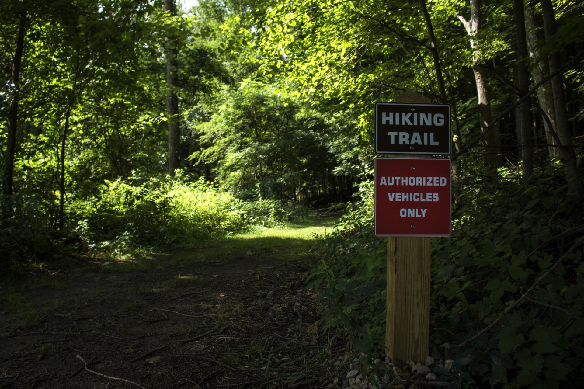 A hiking trail sign reading "HIKING TRAIL" and "AUTHORIZED VEHICLES ONLY" posted on a wooden post alongside a wooded path.