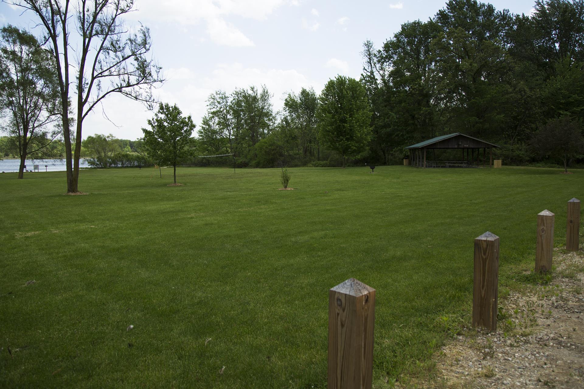 Open grassy park area with wooden posts, shelter building, trees, and water visible in background.