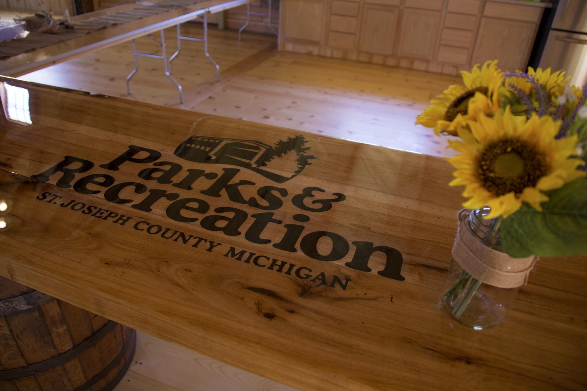 Parks & Recreation sign for St. Joseph County Michigan on wooden counter with sunflowers in a vase.