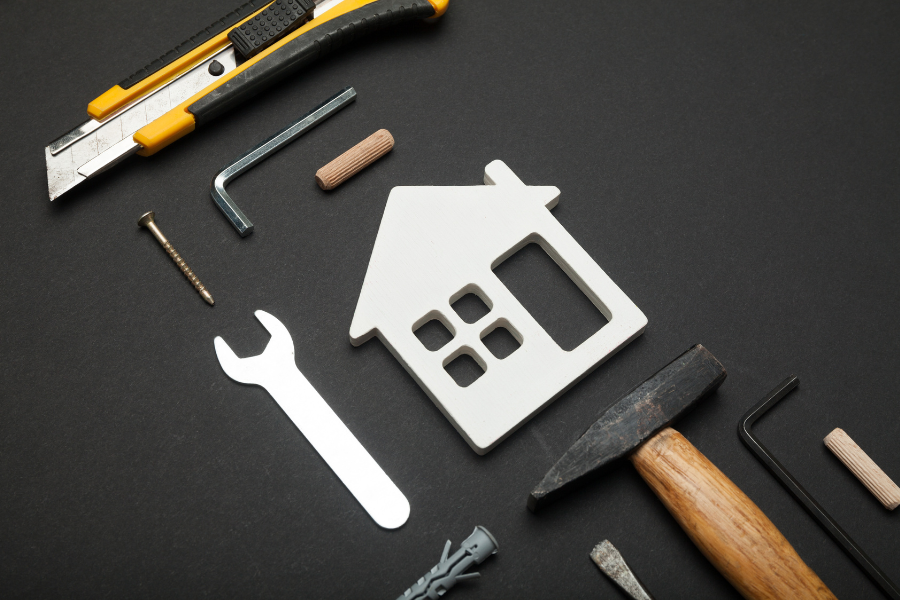 Flat lay of home repair tools arranged around a white house-shaped icon on dark background.